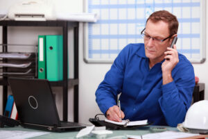 Man in office talking on the telephone and writing notes in a book.