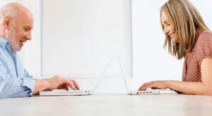 Man and a woman sit facing with laptops between them.
